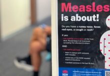 Australiens mässlingsskydd utmanas – svenskt utbrott blottar riskerna med sviktande flockimmunitet En person i Australien sitter bredvid en skylt om spridandet av mässling.