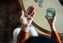 Färre antibiotikarecept – men ingen ökning av allvarliga infektioner Person med glas i ena handen och tabletter i andar handen.
