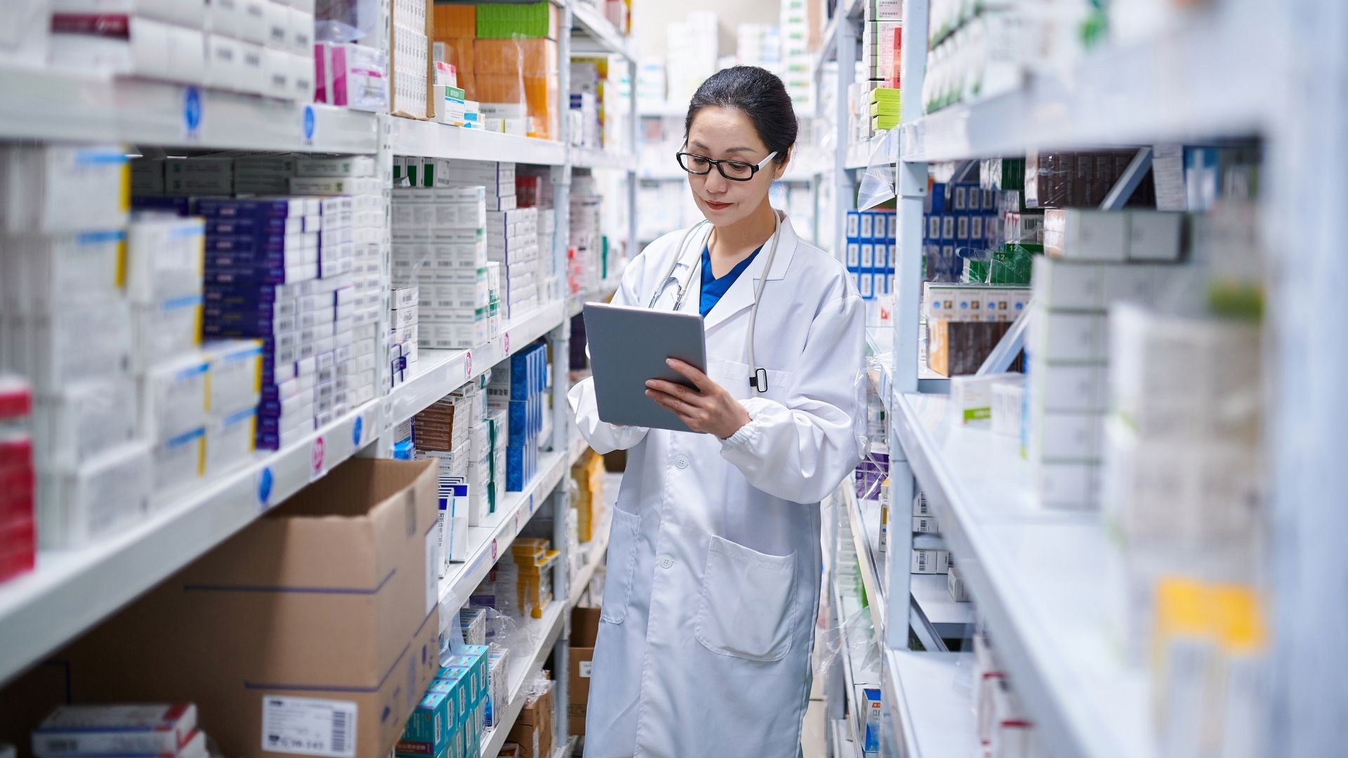 Apotekare med anteckningsblock bland hyllor med medicin till artikeln om läkemedelsförsörjningen i Sverige.